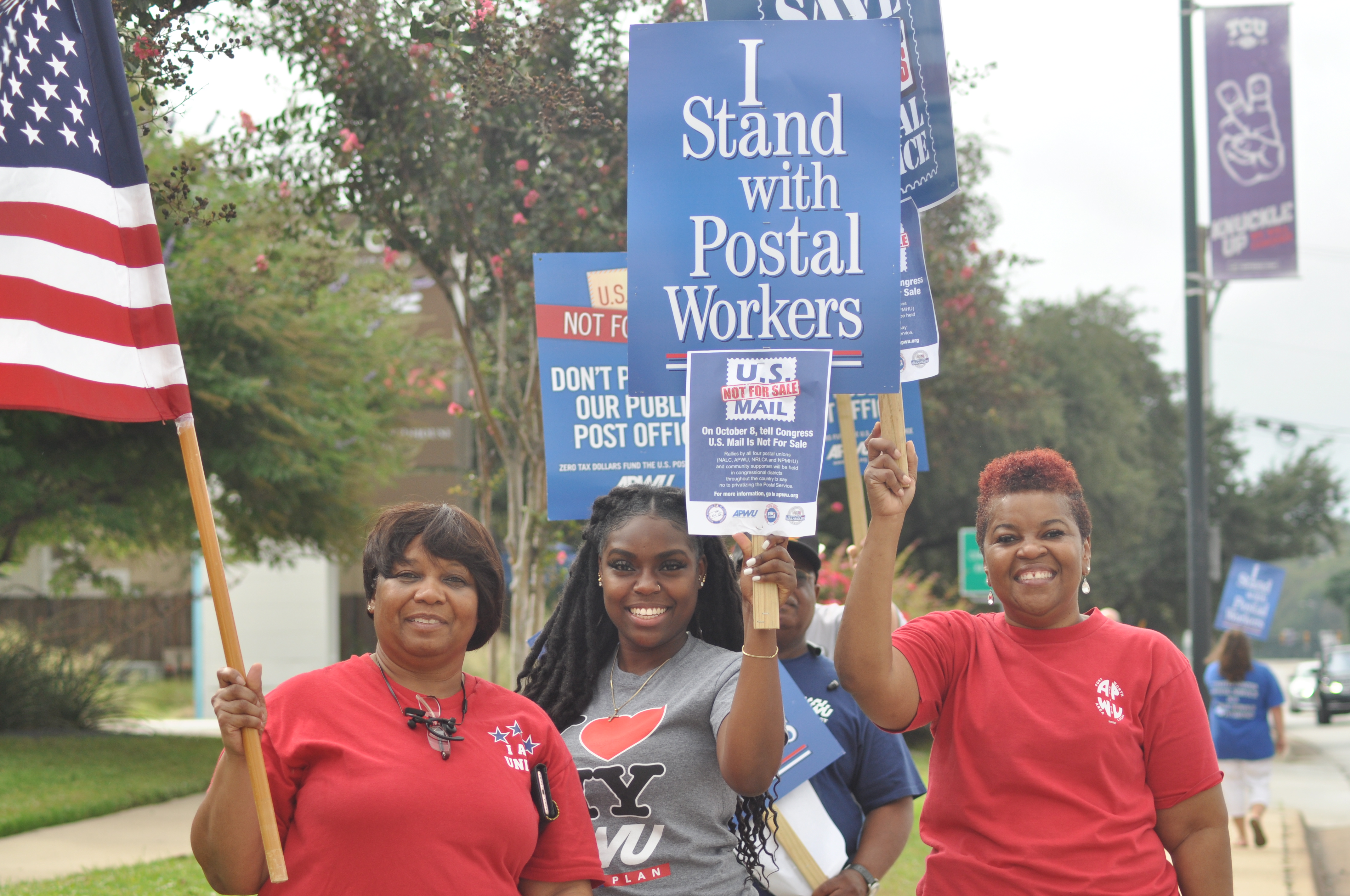 Postal workers holding up an American flag and signs that say U.S. Mail is Not For Sale!