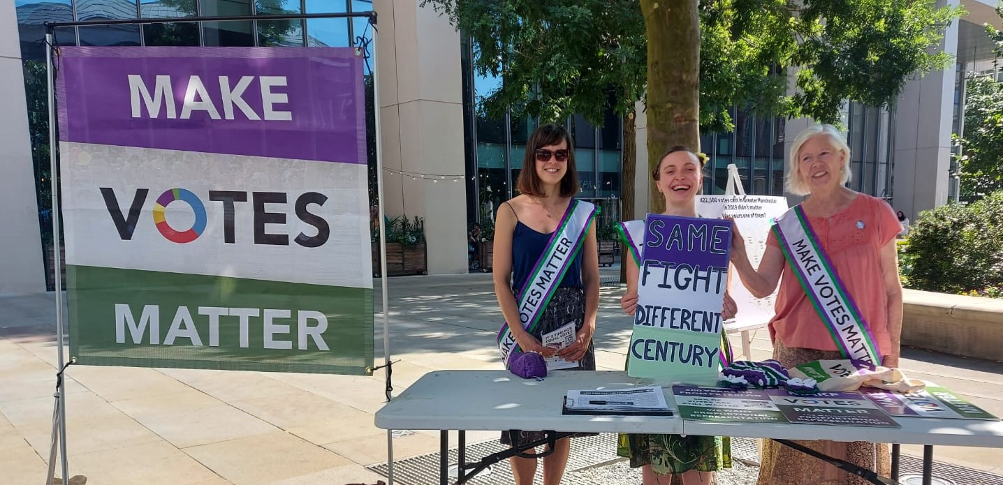 Image shows people standing by a Make Votes Matter information stall.