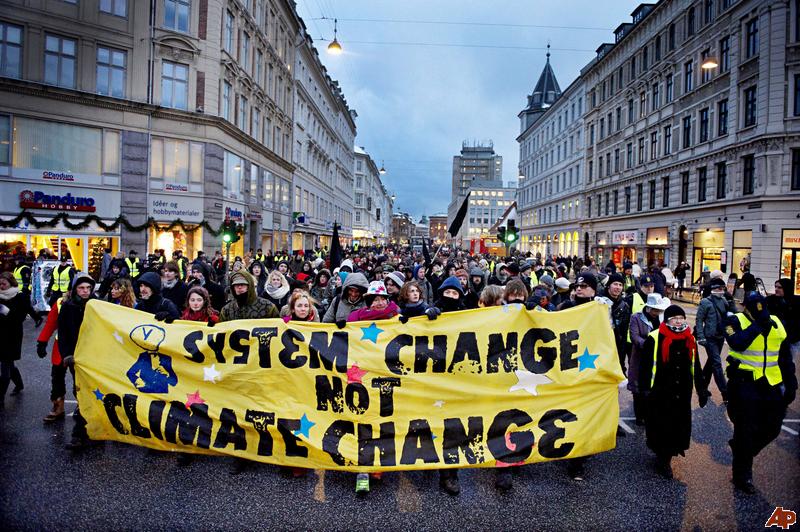 An image of a climate protest featuring protestors holding a yellow banner reading "SYSTEM CHANGE NOT CLIMATE CHANGE"