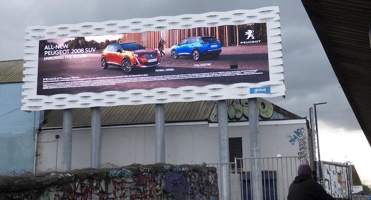 An advert for SUV cars on a large digital billboard on tall legs outside a warehouse building