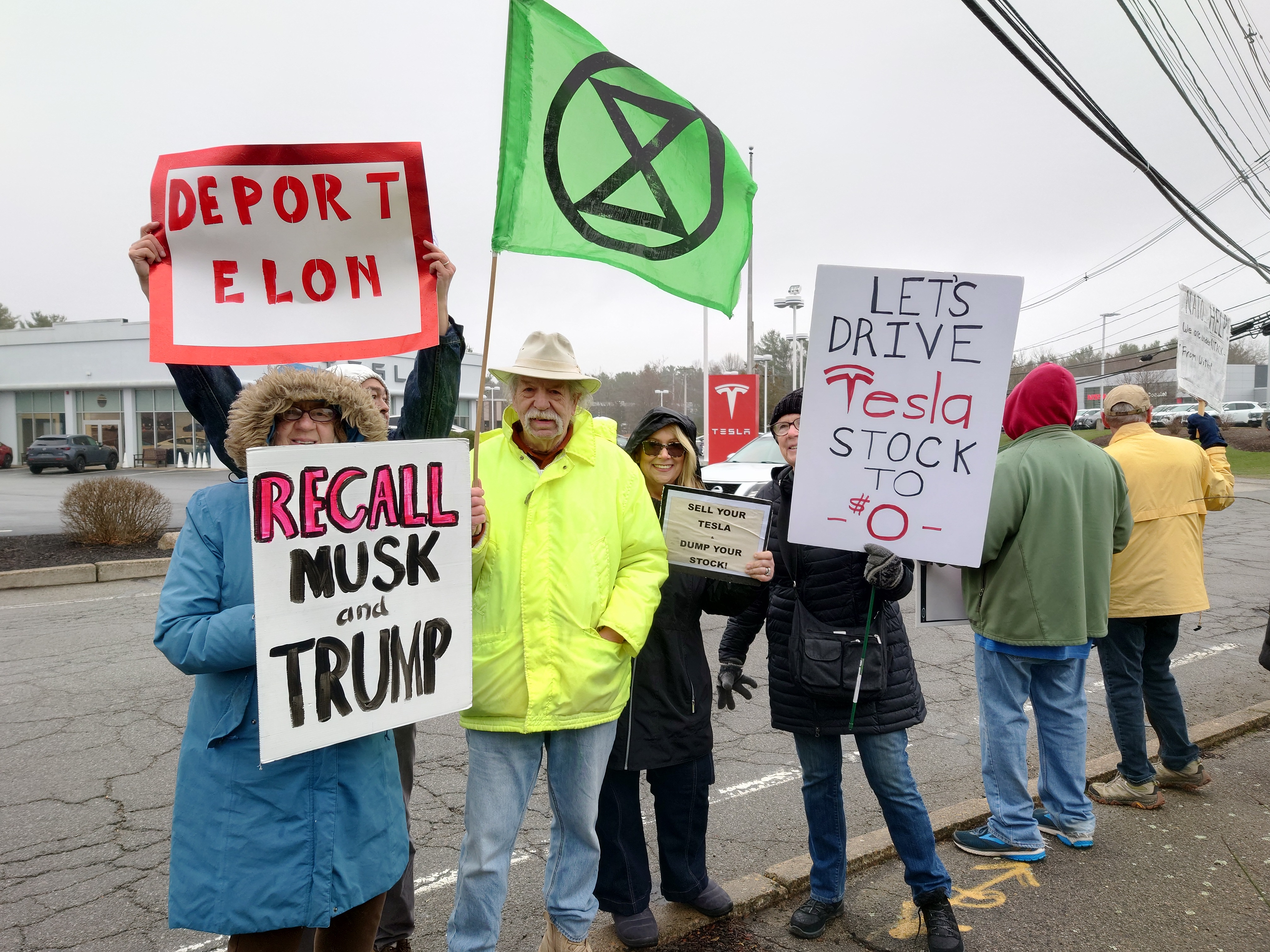 view demonstrators with signs in front of a Tesla showroom from across the roadway