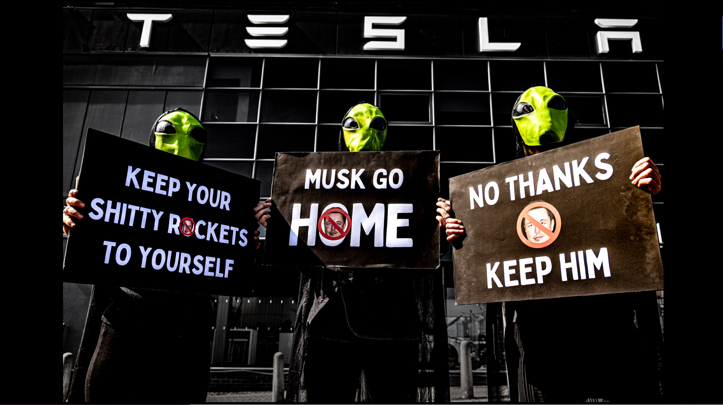 Three martians against a Tesla holding signs reading Musk Go Home, Keep Your Shitty Rockets to Yourself and No Thanks, Keep Him