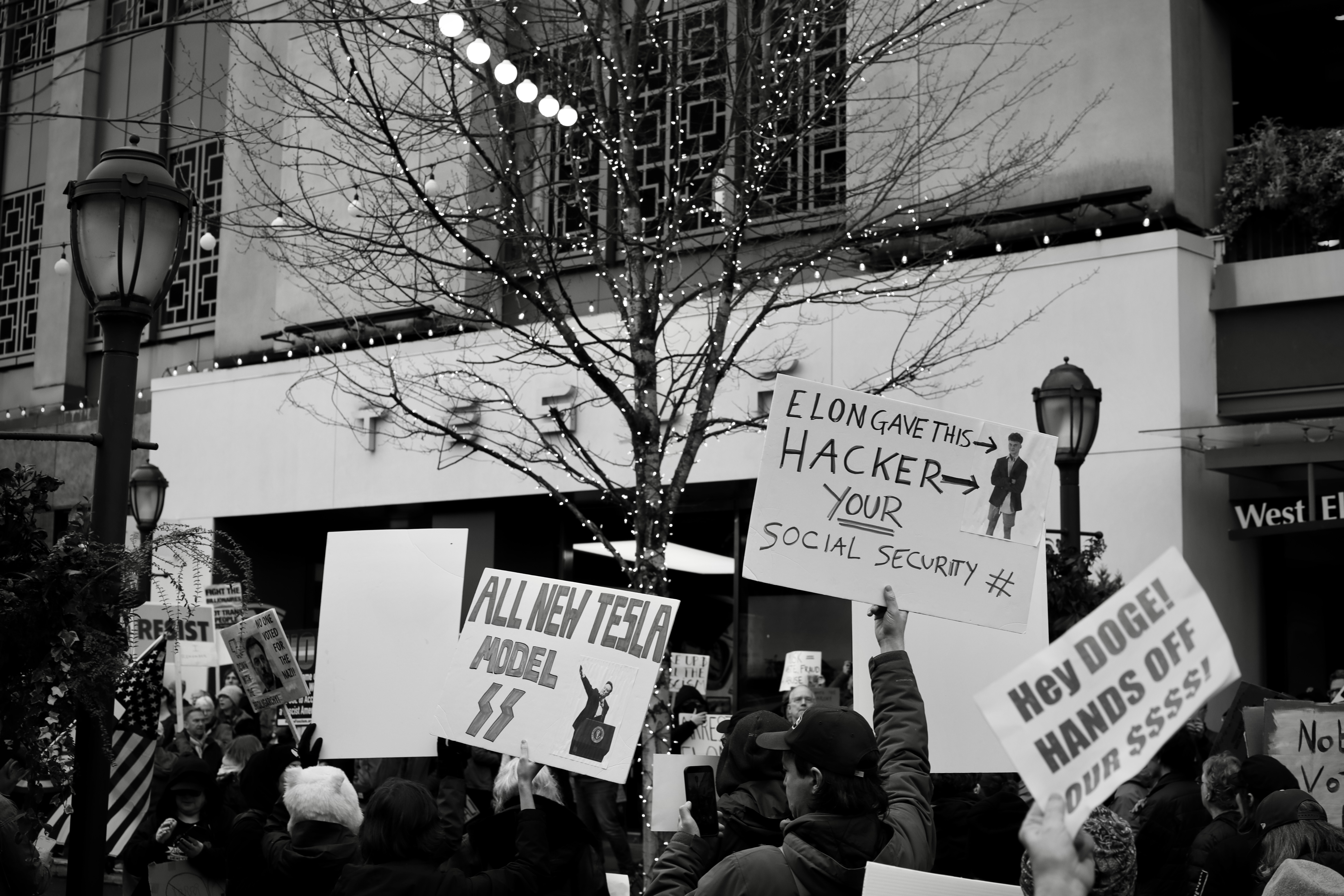 Protestors hold signs in front of Tesla's U Village store