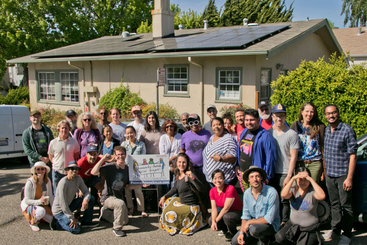 Picture of a group of people smiling in front of a small building with solar on the roof