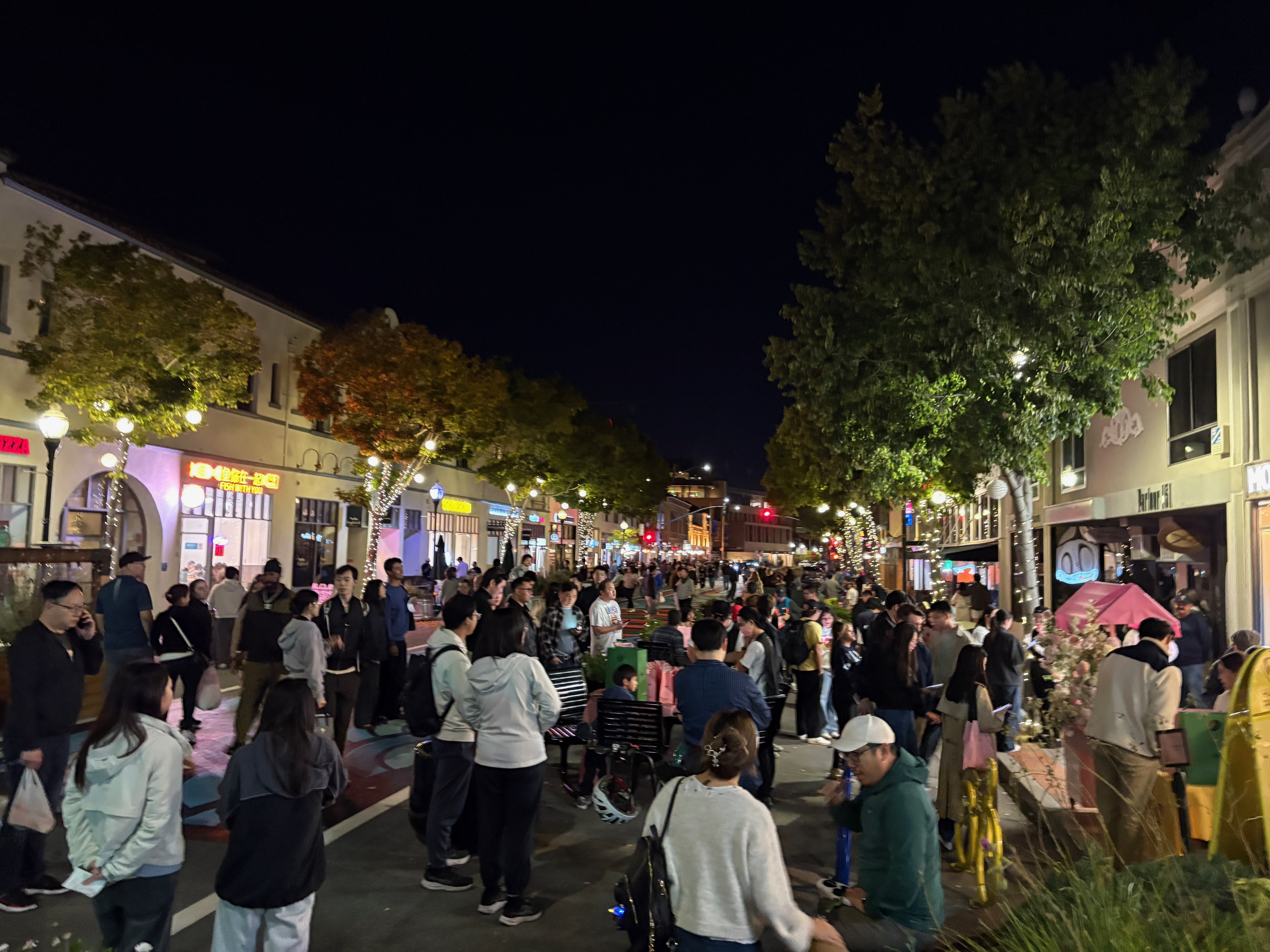 A photo of downtown San Mateo's B Street pedestrian mall at night, crowds of people seated & on foot