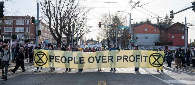 People carrying large, green banner that says "People Over Profit" in front of a crowd of MLK marchers