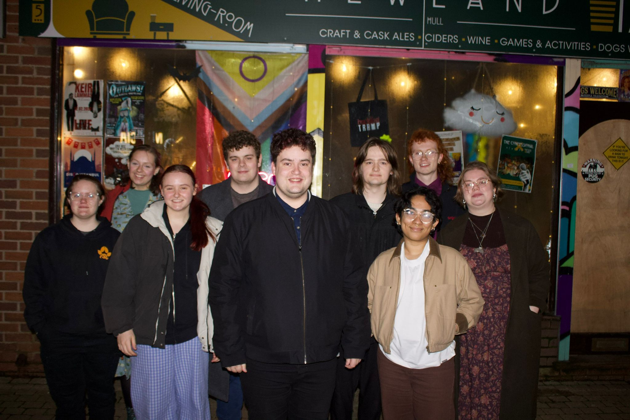 Members of H&ER Green Party stand with Jamie Strudwick outside a local venue. A Pride Progress flag is displayed in the window.
