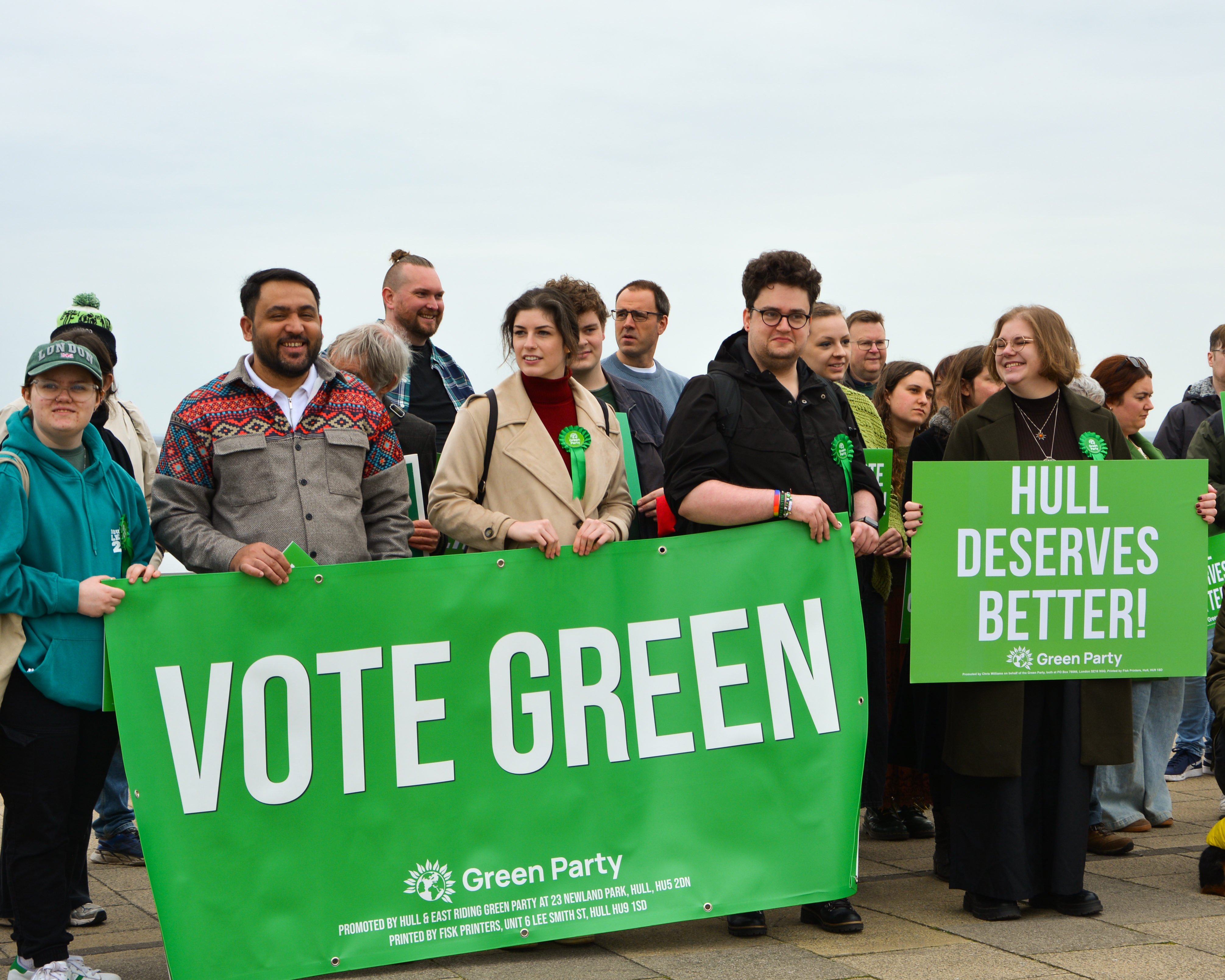 Members of H&ER Green Party stand outside by the River Humber. They are holding a large banner which says VOTE GREEN, and a woman on the right holds a board reading HULL DESERVES BETTER. 