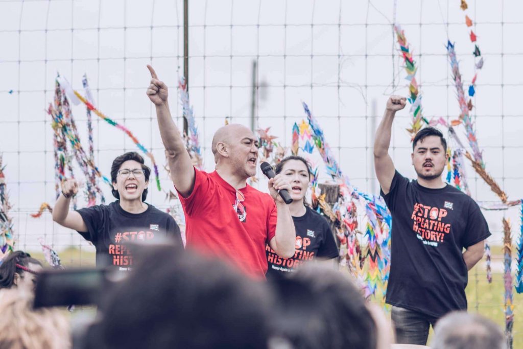 Photo of Japanese Americans with their fists raised outside a family detention center