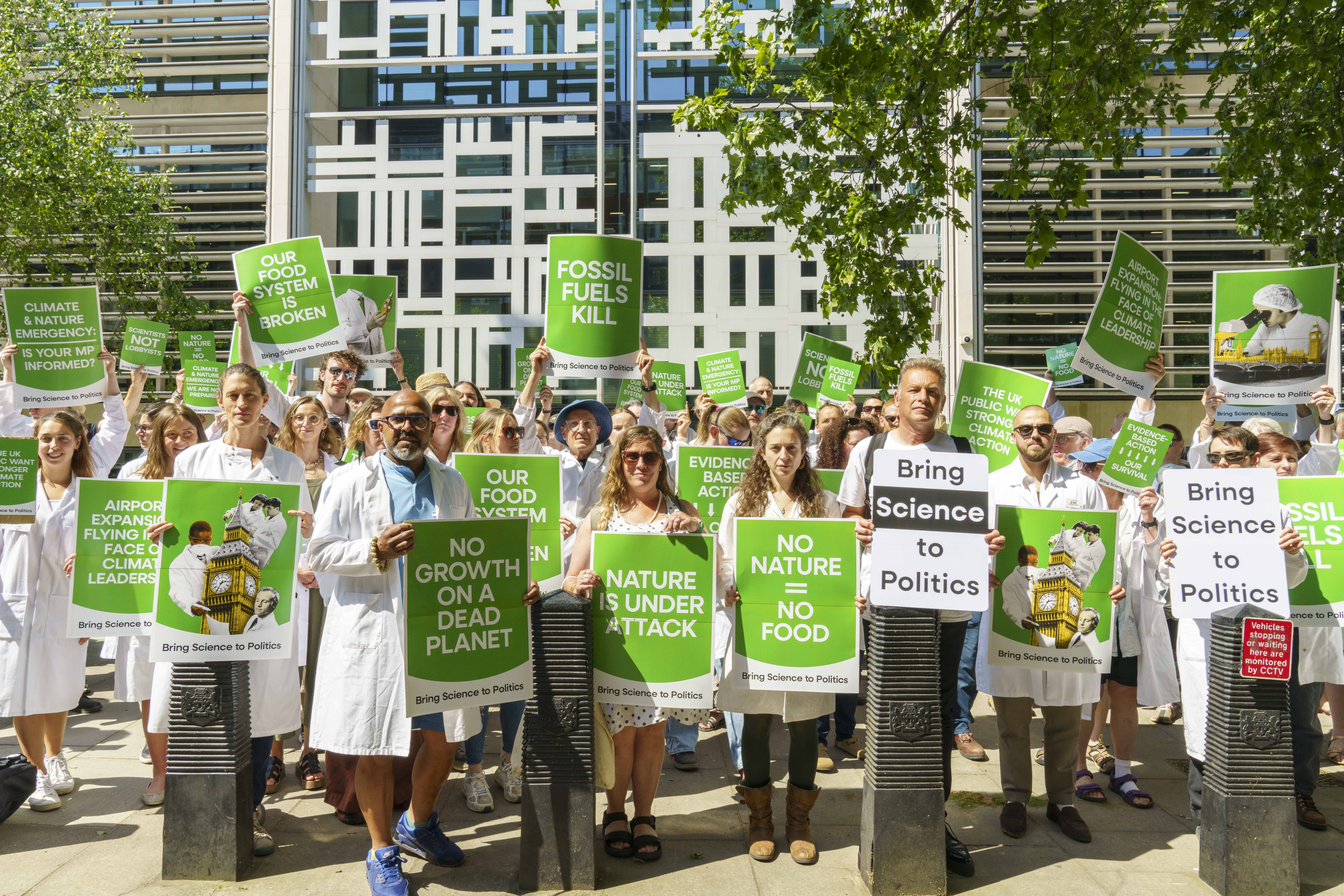 Sceintists in white lab coats holding signs advocating for climate and nature action
