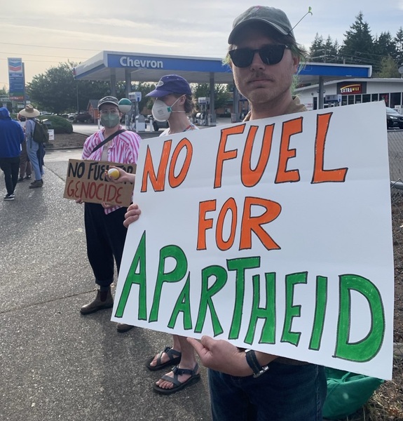 Protester holds sign reading "No Fuel for Apartheid" outside Chevron station