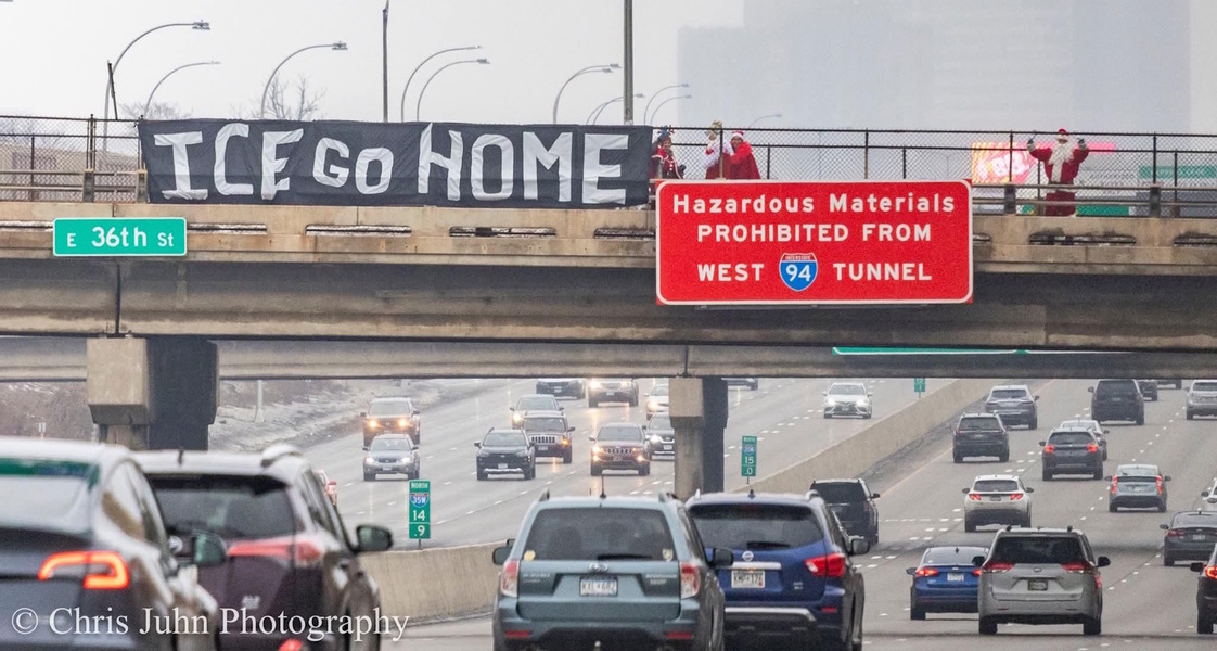 A photo of 3 people dressed in Santa holiday apparel on Christmas day.  They are displaying a banner over 35W that reads "ICE GO HOME"
