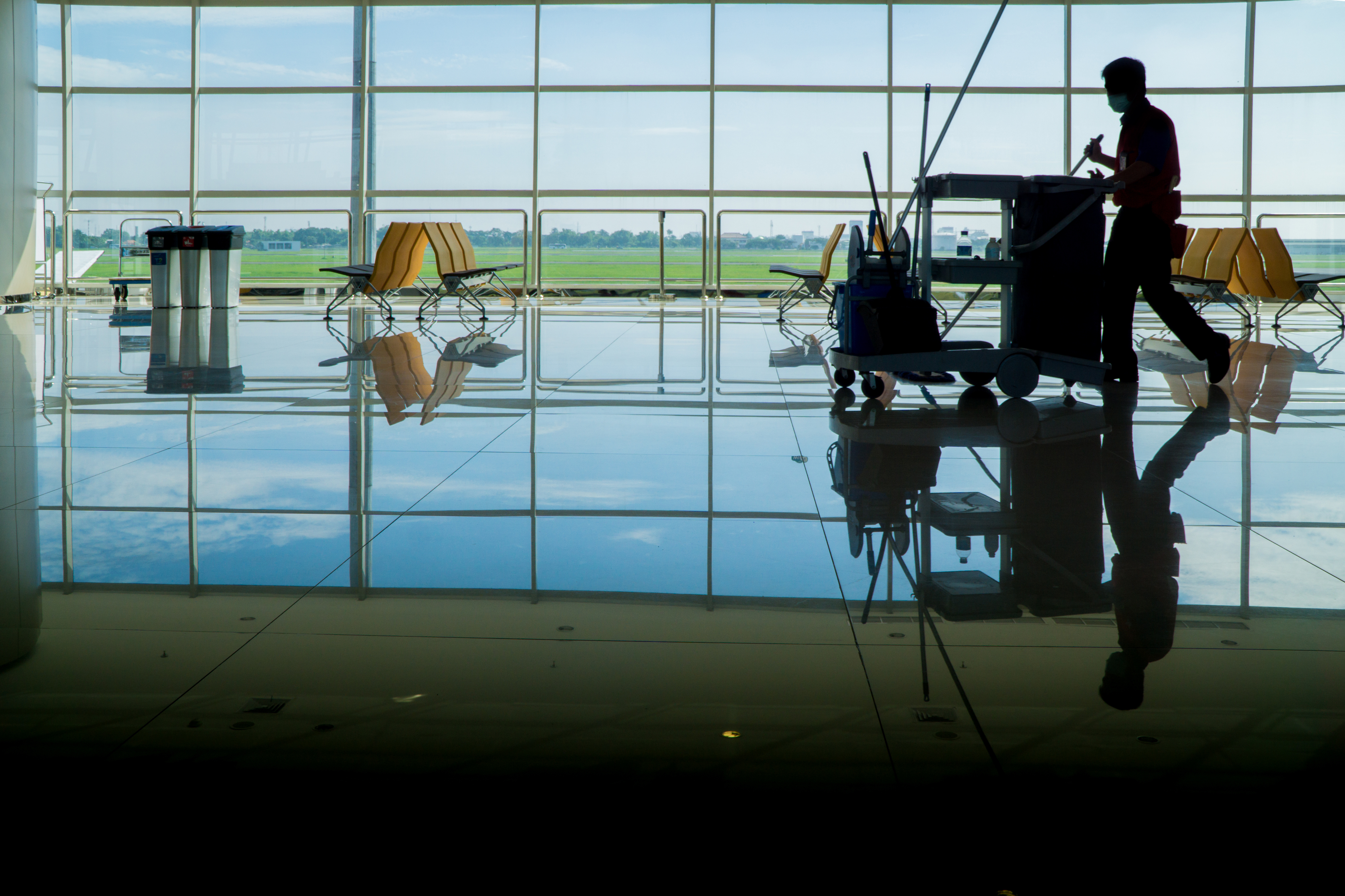 Custodian pushing work cart in airport terminal in front of large windows