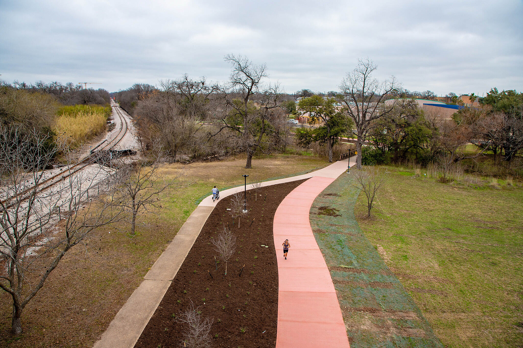 An red bikeway next to a sidewalk and train tracks.