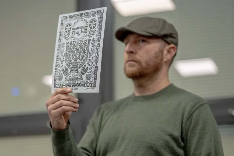 ETHS Teacher Andrew Ginsberg holds up Liora Ostroff's poster featured in Jewish Currents magazine.