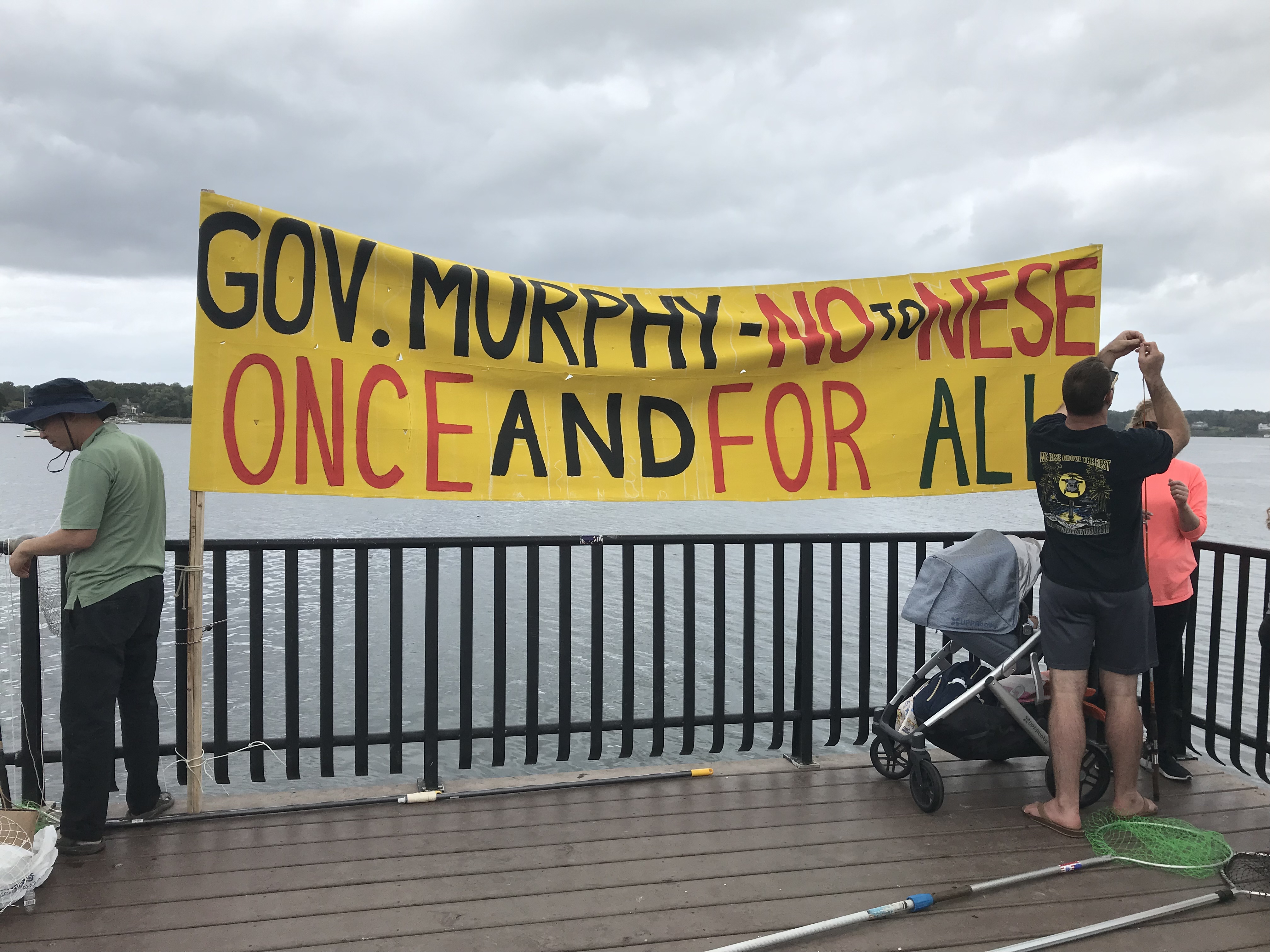 Large banner along the Navesink River Urging Gov Murphy to Stop Nese Once and for All, baby stroller and couple pictured alongside