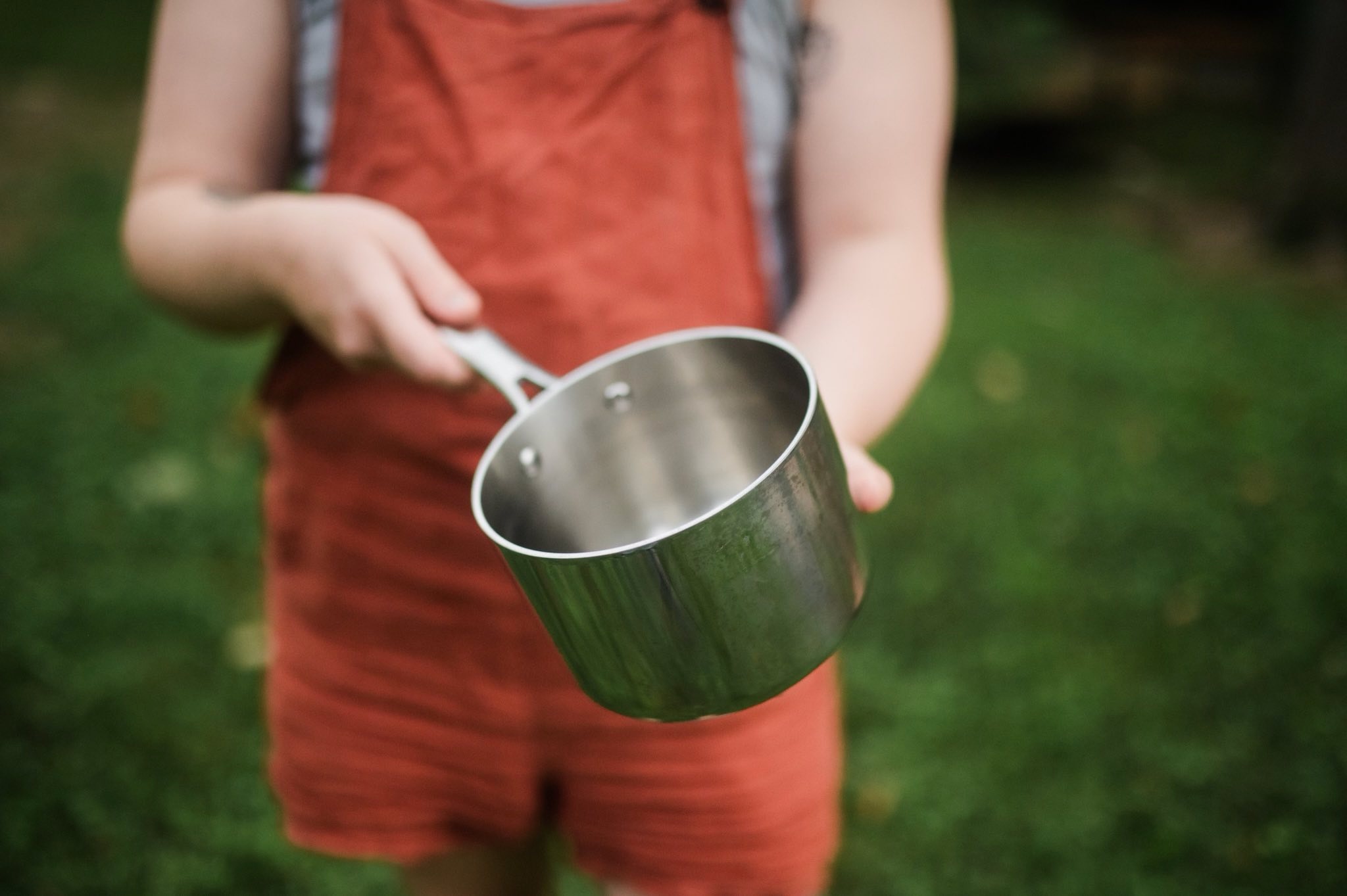 image of a white skinned person wearing a gray tank top and dirt orange overalls holding an empty pot