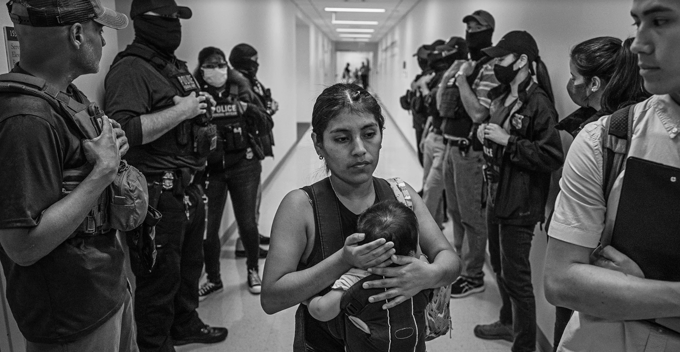 A woman with an infant walks through a corridor of ICE agents. A Photographer’s View of ICE’s Relentless Courthouse Arrests.