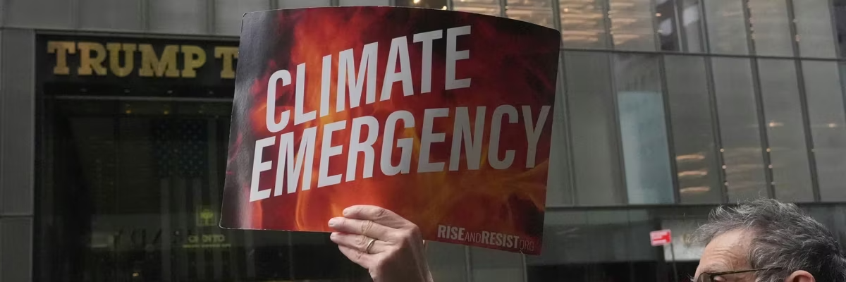 Person holding climate emergency sign in front of Trump Tower