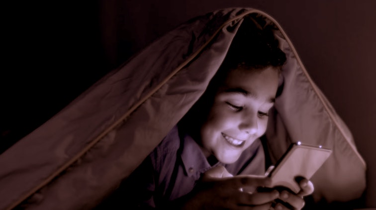 smiling kid playing game on phone under blanket