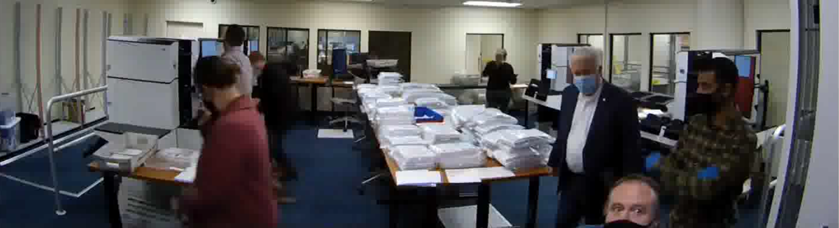 Crowded room in election office with piles of ballots being scanned