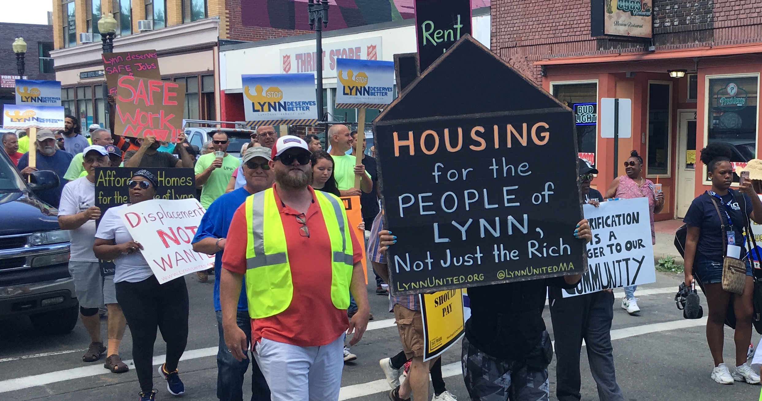 Photo of protest march. Prominently featured sign says, "Housing for the people of Lynn, not just the rich"