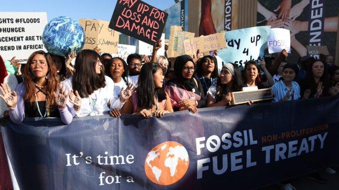 a group of activists from Pacific island nations march behind a banner that says 'we need a fossil fuel non proliferation treaty
