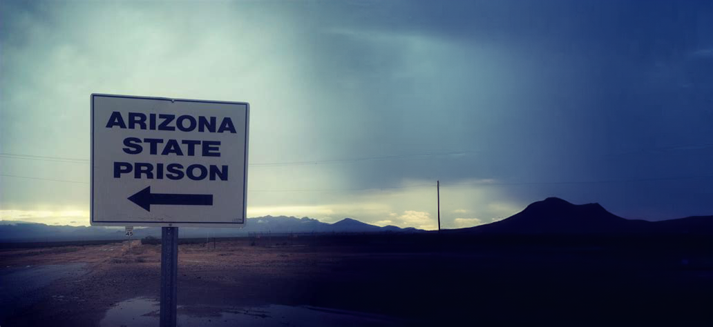 a road sign say Arizona Prison with a storm brewing behind