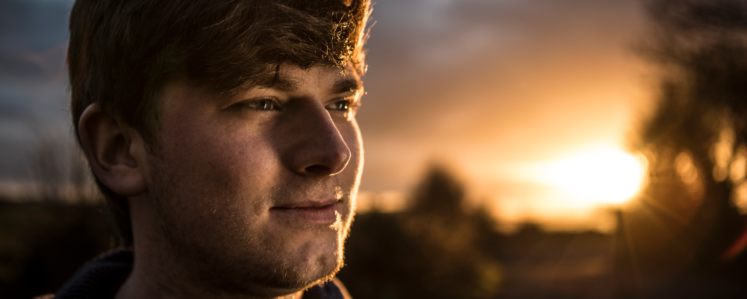 Young man smiling in front of a horizon over a country gate