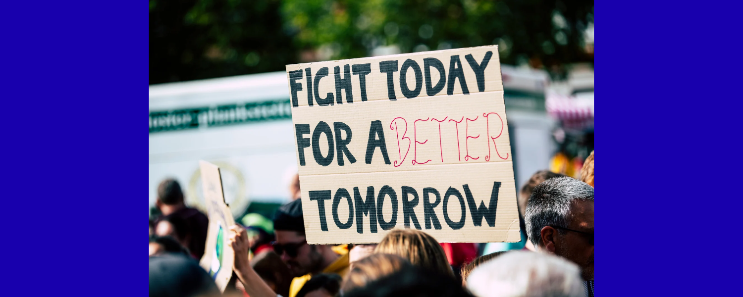 A group of people outside of a building. One is holding up a sign that say "Fight Today for a Better Tomorrow"