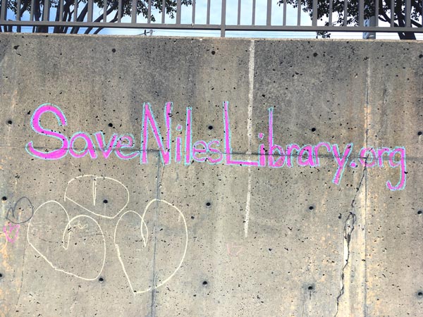 A message written in chalk on a wall that reads Save Niles Library .org.