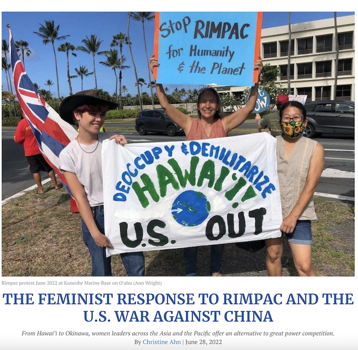 Three activists at the Kaneohe Marine Base on O’ahu hold signs that read "Deoccupy & Demilitarize Hawai'i / U.S. OUT" and "Stop RIMPAC for Humanity & the Planet"