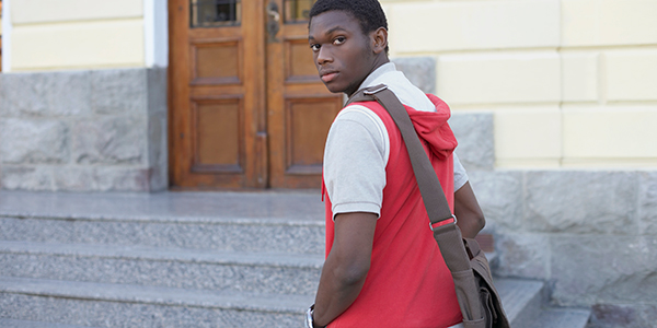 A young man with a courier bag going up school steps, looking over shoulder at the camera