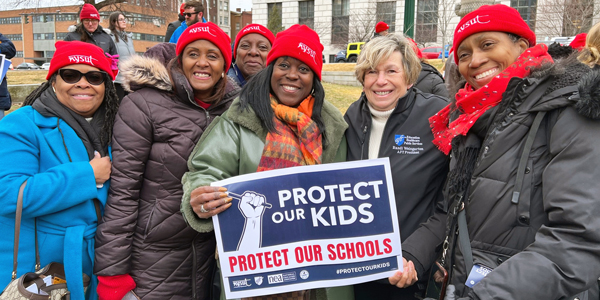 Randi Weingarten with protesters with a sign "Protect Our Kids"