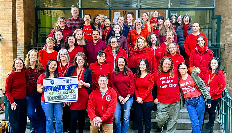 Big group of teachers in red t-shirts on the steps of a school