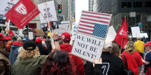 Crowded street protest with sign that reads, "We will not be silent"
