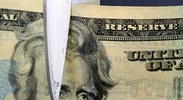 A pair of scissors cuts through a twenty dollar bill.