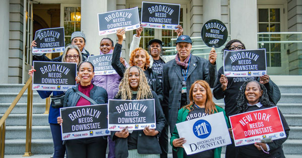 A group of people standing with sings that read "Brooklyn needs Downstate."