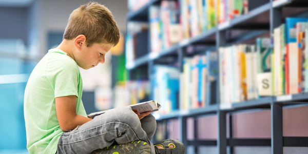 Boy sitting cross-legged beneath library stacks | Photo credit: vm/GettyImages