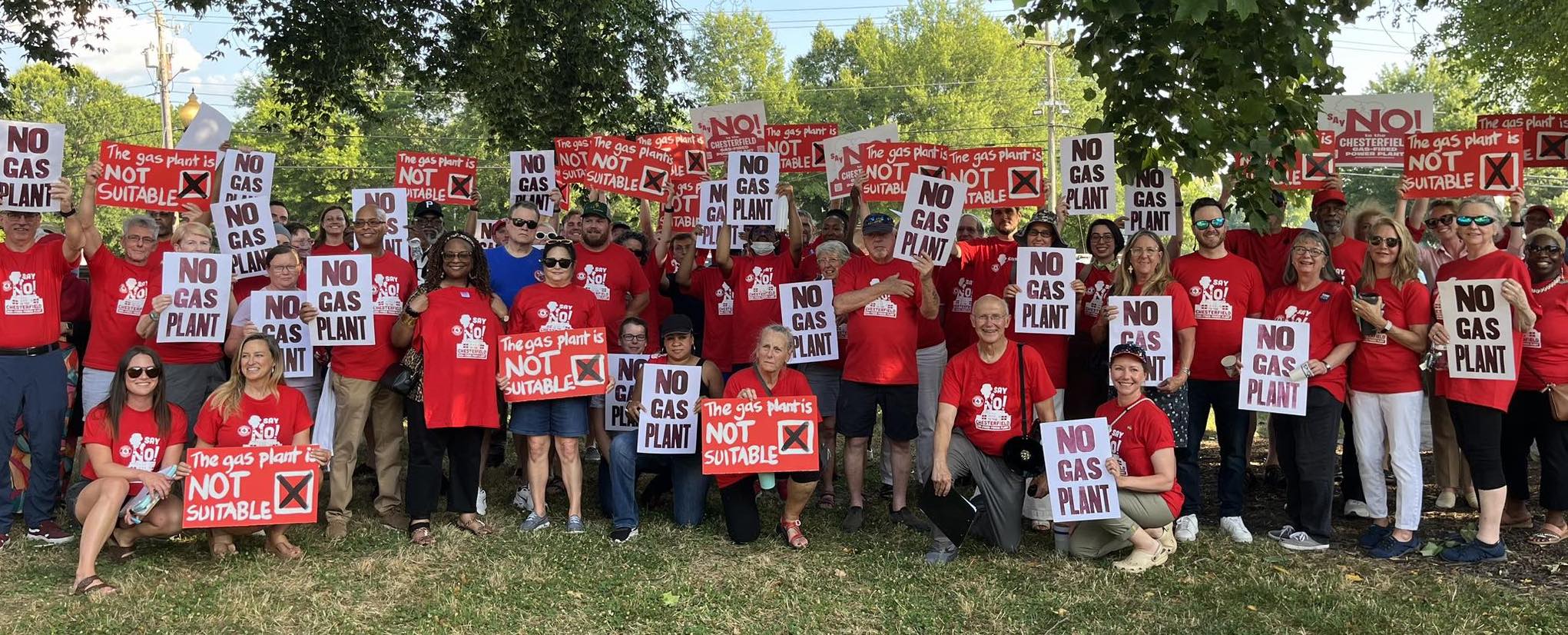 Community members wearing red shirts and holding signs protesting the gas plant