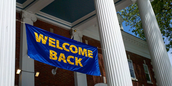Blue and yellow "welcome back" banner hanging on a columned building