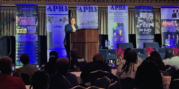 Randi Weingarten speaking at the podium with APRI signs behind her