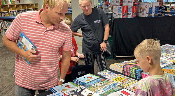 Two adults and a child looking over books on a table