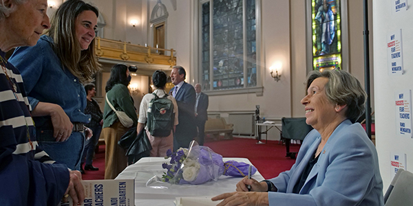 Randi Weingarten smiling at two people facing her, looking up from a table where she is signing books