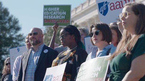People standing in protest with a sign, "Higher Education Research Saves Lives" People standing in protest with a sign, "Higher Education Research Saves Lives"