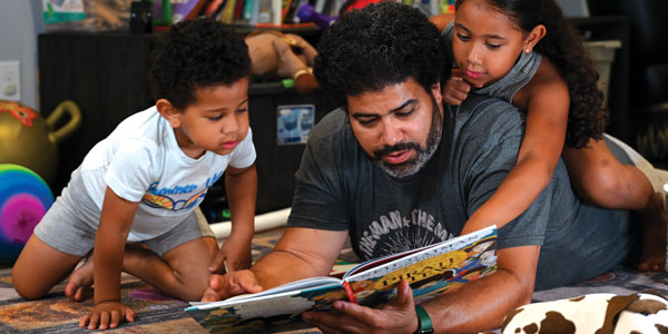 A man reading to two children on the floor