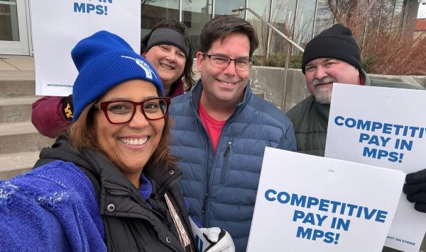 Four educators smiling outdoors with signs that say "competitive pay in MPS"