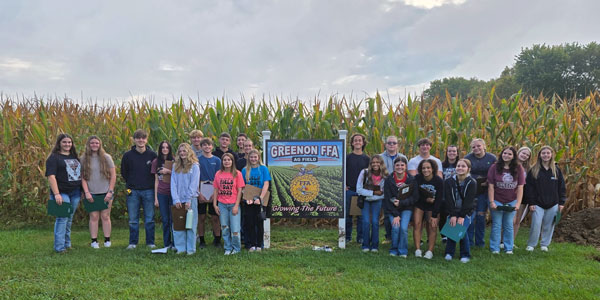 a large group of students standing in front of a corn field with a sign, "Greenon FFA"