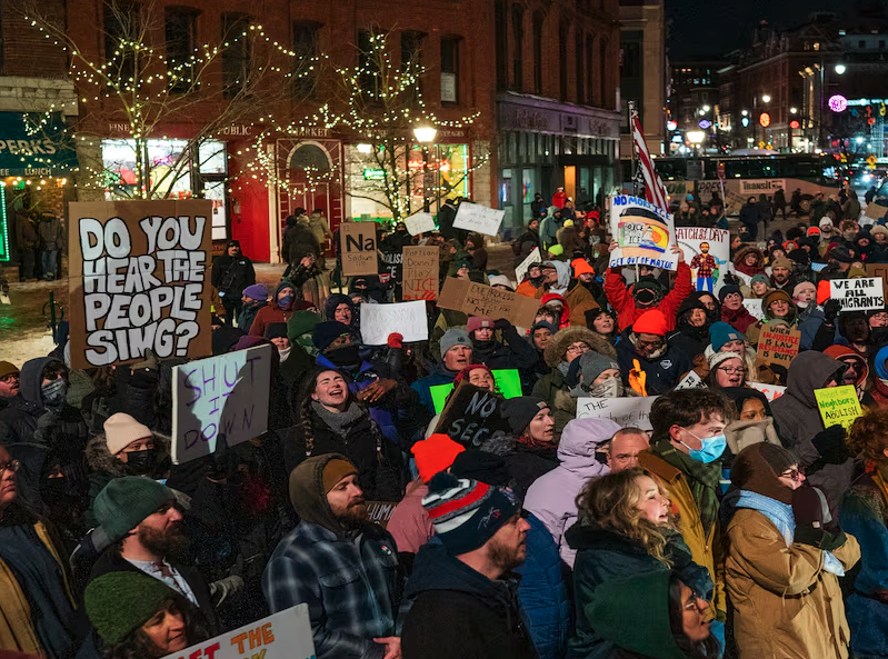 Protestors in Portland, Maine, one with large sign reading 