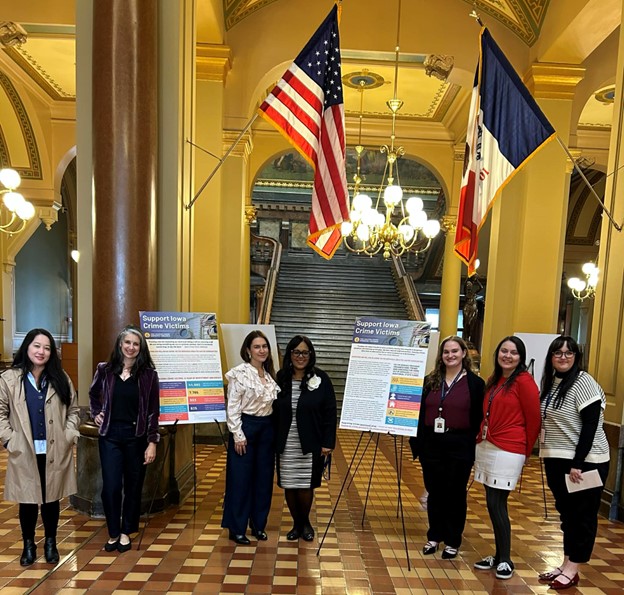 Representative of The Iowa Coalition Against Domestic Violence stand with Senator Hardman in front of posters that say "Support Iowa Crime Victims" in the Capitol Rotunda.